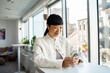© Marko Geber - Smiling young Asian business woman using smartphone in office