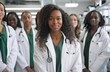 © trustmastertx - A group of young female doctors in white coats stand together, the backdrop is an office with medical equipment visible on the shelves behind them. They come from different ethnicities