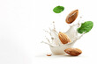Almond with green leaves flying in milk splash isolated on white background. Nuts in organic vegan liquid.