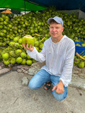 Fototapeta Koty - A man holds a green coconut with a straw in his hand at the market