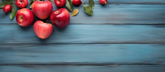 Wall Mural - A copy space image featuring a rustic wooden board adorned with a heart leaves and an arrangement of vibrant red apples set against a backdrop of a serene blue background