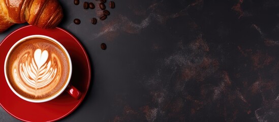 A top view of a cappuccino or latte in a red cup alongside a chocolate croissant on a dark marble background Perfect for breakfast with copy space for text