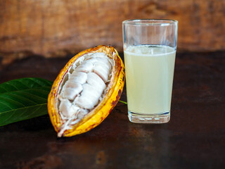 Wall Mural - Fresh cacao water in glass and half sliced ripe yellow cacao pod with white cocoa seed, Cacao juice in glass  on vintage wooden background