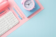 A tidy workstation featuring a white keyboard, pink alarm clock and various stationery items on a dual-toned pastel background