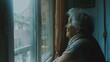Elderly woman gazes out raindrop-covered window, contemplative