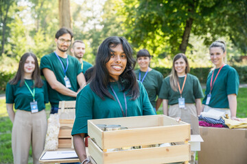 Wall Mural - Portrait of a young woman with a group of uniformed volunteers behind her during a food bank charity event, donating basic necessities for the needy