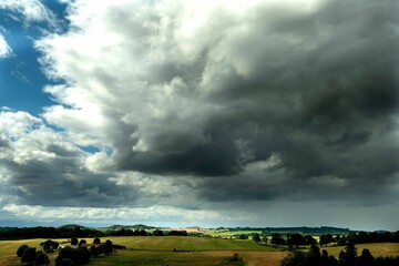 Wall Mural - Landscape featuring a cloudy sky and lush green fields of grass and trees in the background.