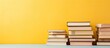 © Gular - A copy space image shows an open book placed on top of a stack of books The vibrant pastel yellow background adds a warm and inviting atmosphere evoking feelings of learning education and the start o