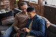 © ReeldealHD images - Gay couple at home sitting on a sofa looking at a smartphone together