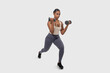 © Prostock-studio - Black woman is standing on a white background, lifting dumbbells with both hands. She is focused and determined, showcasing strength and endurance during her workout routine.