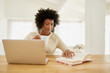 © peopleimages.com - Woman, laptop and happy in home with book, social media and typing or browse for online shopping or networking. Communication, internet search and reading novel on weekend, relax and apartment table