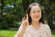 Healthy happy smiling middle aged asian woman pointing 1 fingers up, concept of one point, number one in summer green park