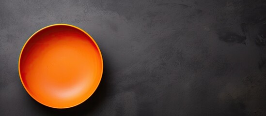 An empty orange dish with a matte finish is seen from a top view resting on a dark cement background There is copy space available for your design