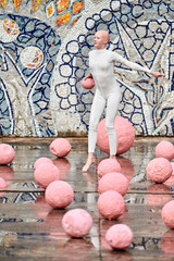 Wall Mural - Young hairless girl ballerina with alopecia in white futuristic suit dancing outdoor among pink spheres on abstract mosaic Soviet background, symbolizes self expression and acceptance of unique beauty