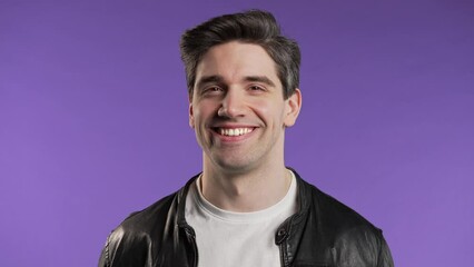 cheerful man winking with eye, flirting and smiling to camera on violet studio