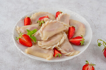 Wall Mural - Tasty traditional dumplings, varenyky or pierogi with strawberry and sour cream on a white plate.