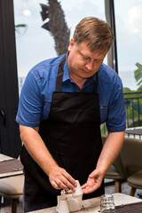 Wall Mural - A blond male waiter aged 40-44 lays out cutlery on the table.