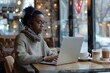 © HendraGalus - Nomad lifestyle concept. Black female working remotely from a coffee shop with her laptop