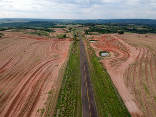 Wall Mural - Aerial drone view of land with a newly planted coffee field being crossed by a paved rural road, in the state of Sao Paulo, Brazil