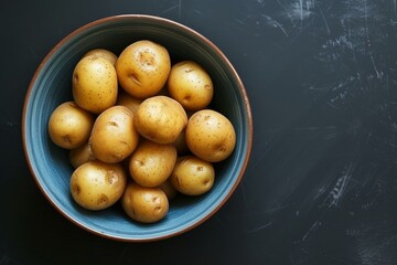 Poster - Top view of ripe yellow potatoes in a blue bowl on a dark background