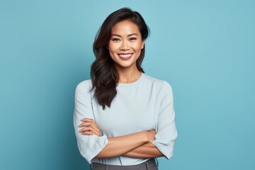 Wall Mural - Portrait of a glad asian woman in her 30s with arms crossed while standing against soft blue background