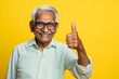 © Markus Schröder - Portrait of a happy indian elderly man in his 90s showing a thumb up while standing against soft yellow background