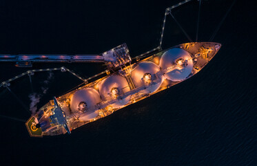 aerial of liquified natural gas lng carrier moored to a small gas terminal at night. fuel crisis. sa