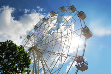 Ferris wheel against the background of blue sky and trees.