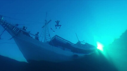 Poster - Underwater view of the boat in the sea with person jumping into the water from the vessel. Silhouette of the cruise boat as seen from the depth underwater