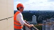 © Nataliya - Happy male builder wearing helmet and protective glasses, standing on the roof, looking at the view. Business, building, industry concept. Slow motion