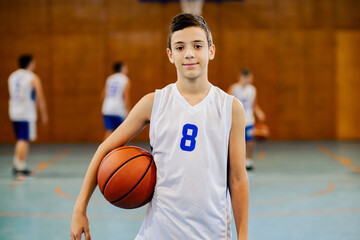 Wall Mural - A junior basketball player standing at court with ball and smiling.