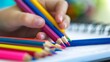 Child's hand holding colorful pencils over notebook. Close-up educational activity and creativity concept for children's book design.