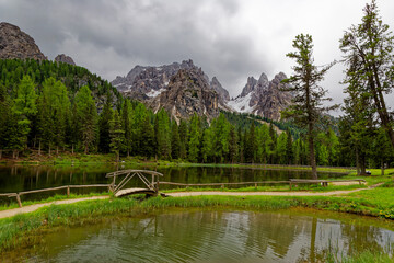 Wall Mural - Green lake in the heart of the Dolomite Mountains. Moody landscape with turquoise water alpine lake Lago di Dobbiaco in Dolomites mountains, Cortina dAmpezzo, Italy on cloudy spring day. Lake Toblache