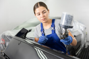 Wall Mural - Young woman mechanic in uniform paints car with machine in car service station