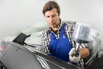 Wall Mural - Adult male mechanic in uniform paints car with machine in car service station