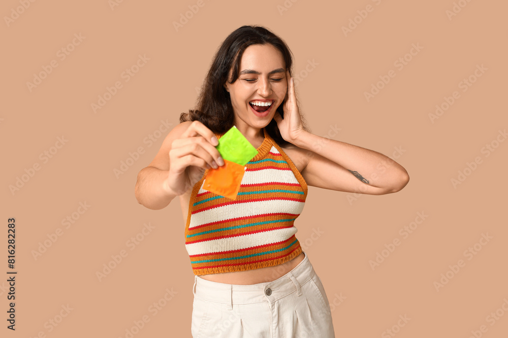 Happy young woman with condoms on beige background. Safe sex concept