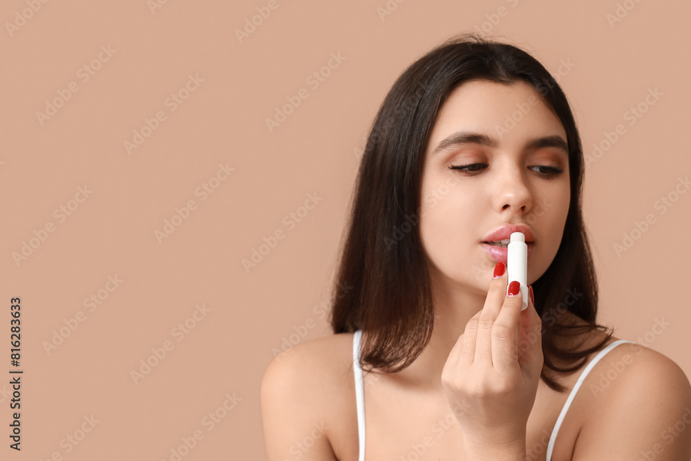 Beautiful young woman applying lip balm on color background