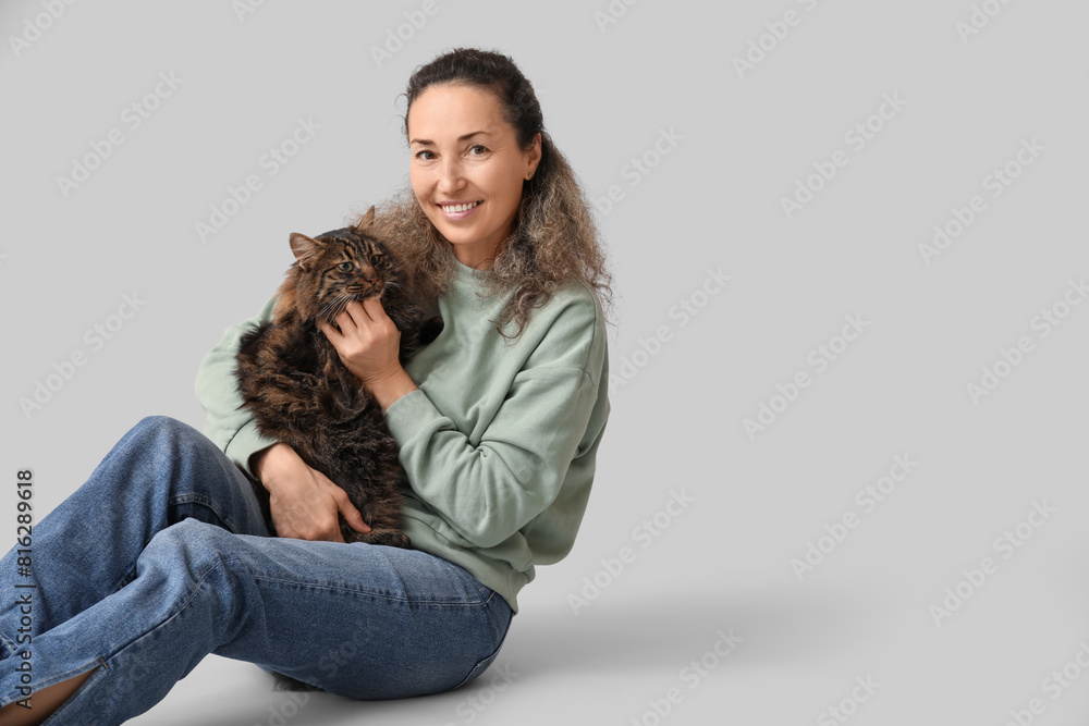Mature woman with cute cat sitting on grey background
