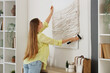 © Pixel-Shot - Young woman hanging 3D painting on light wall at home