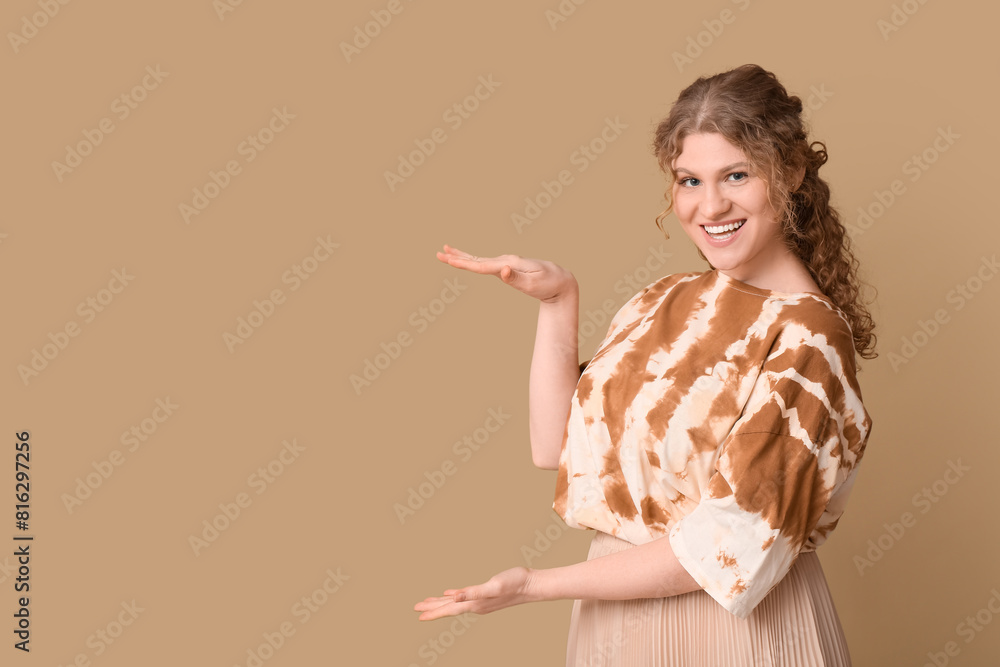 Happy beautiful young woman pointing at something on brown background
