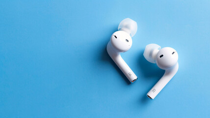 Pair of white wireless earbuds on a bright blue background.