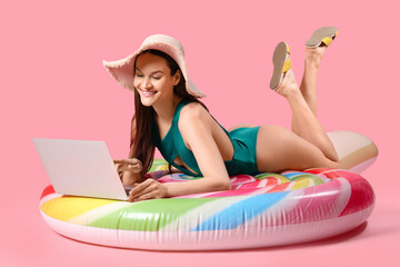 Wall Mural - Smiling woman with laptop lying on inflatable mattress against pink background