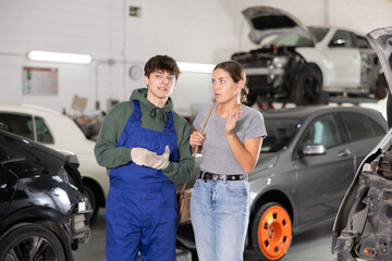 Wall Mural - Young guy mechanic advises young woman client on car repair in car service station..