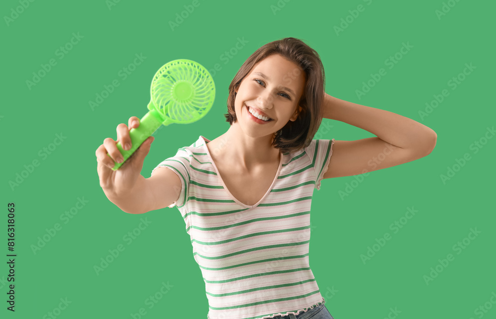 Young woman with small electric fan on green background