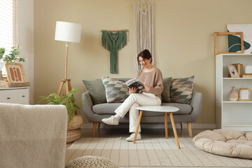 Sticker - Young woman reading magazine on sofa with hanging wall tapestries in living room