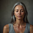© GLH - A woman with prematurely grey hair and closed eyes appears to be meditating against a neutral backdrop.