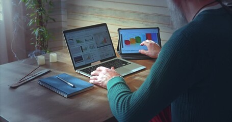 Home Office. A man with a beard analyzes growth charts on a laptop and tablet