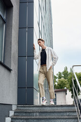 Wall Mural - A young queer person in stylish attire stands confidently on the steps of a building celebrating LGBT pride.
