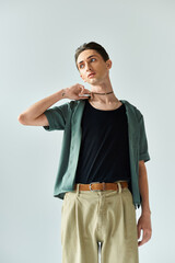 Wall Mural - A young queer person wearing a green shirt and tan pants poses in a studio on a grey background, embodying lgbt and pride.