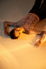 Wall Mural - Young queer person in stylish attire lays on floor, bathed in light, exuding confidence and pride.